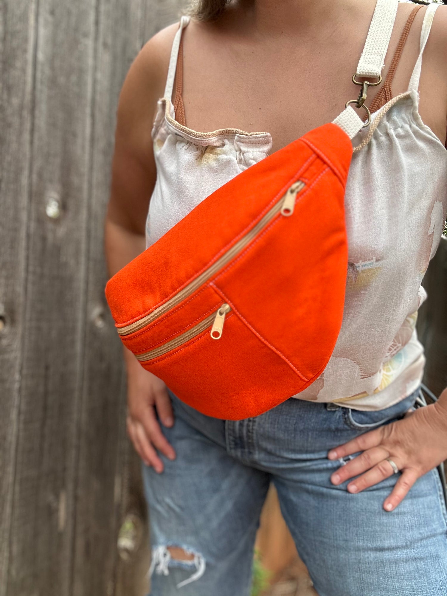 Person wearing an orange waist bag with beige zippers against a wooden background