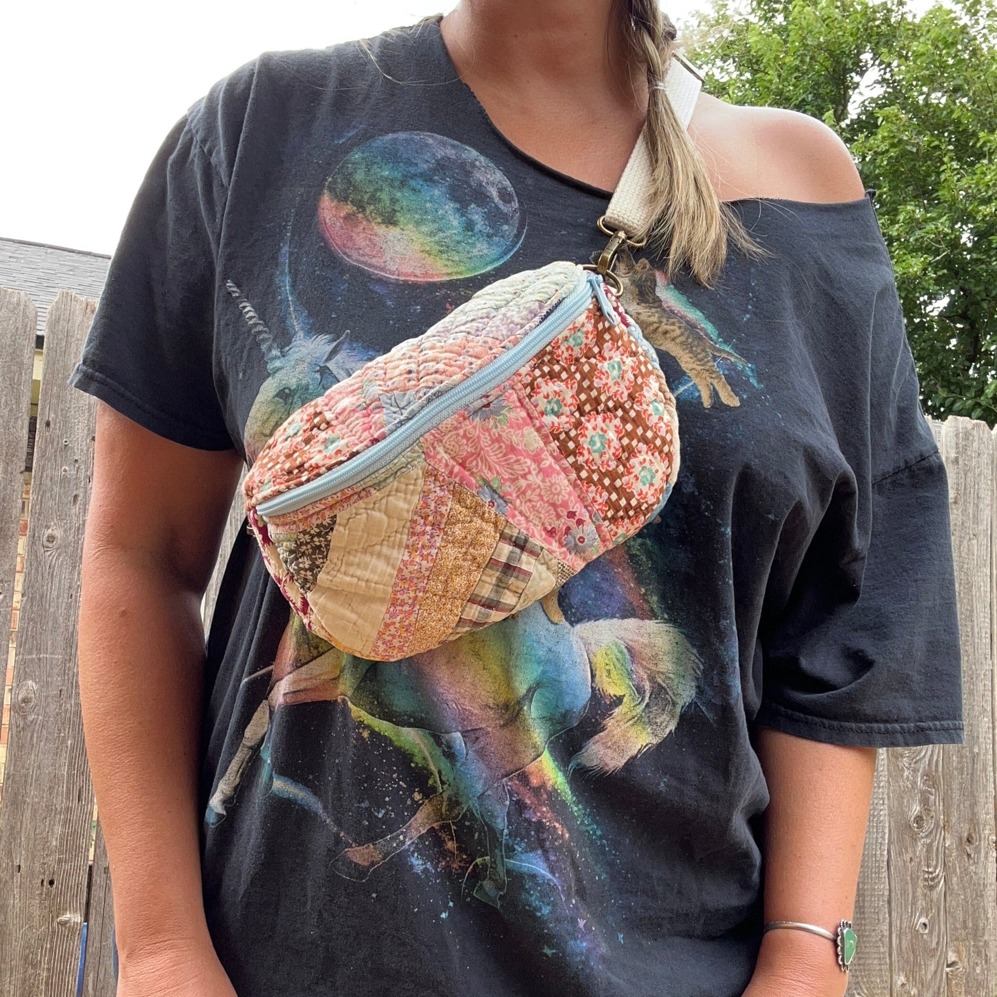 Person wearing a graphic t-shirt with a colorful bag over one shoulder, standing outdoors.