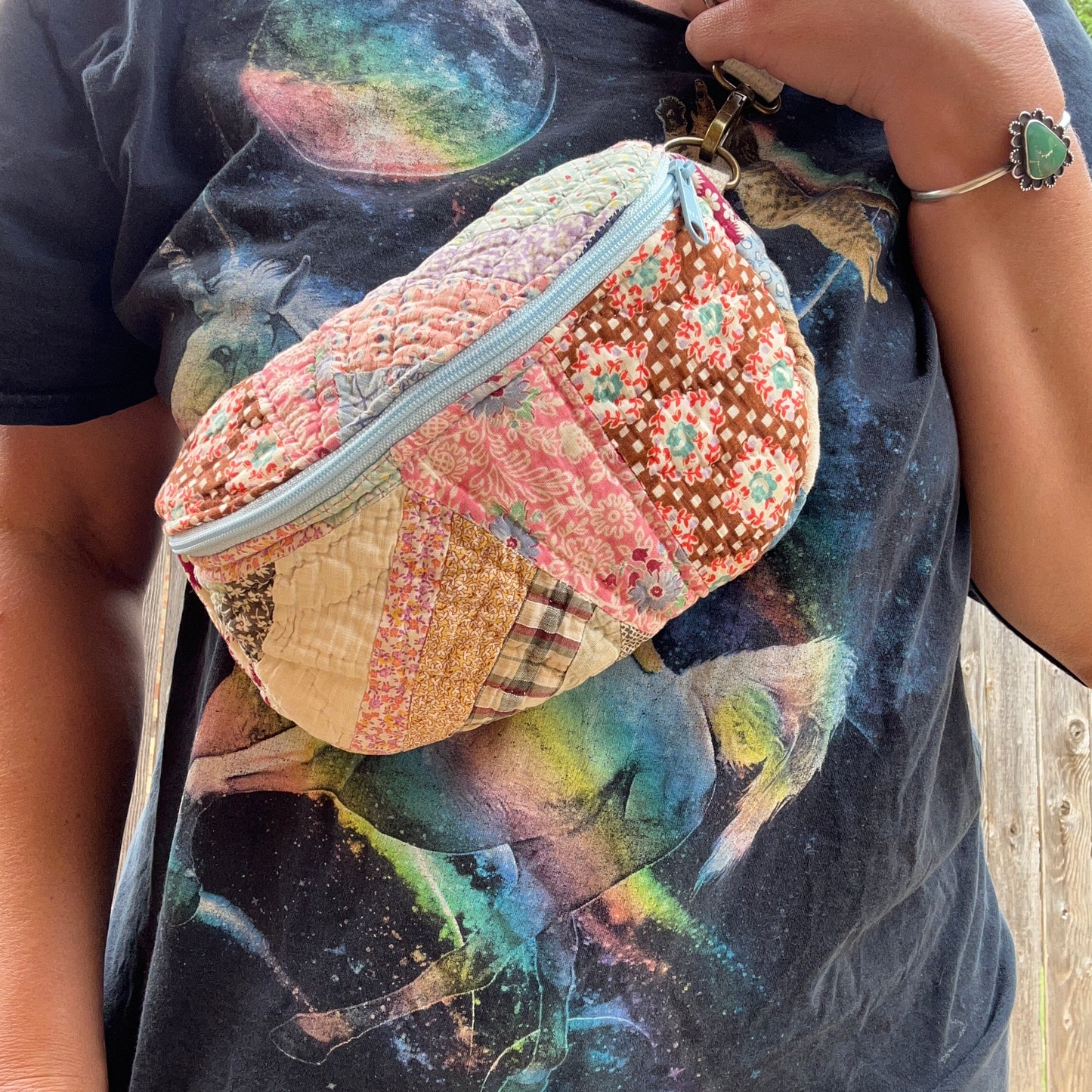 Person wearing a colorful patchwork bag with a graphic t-shirt in the background