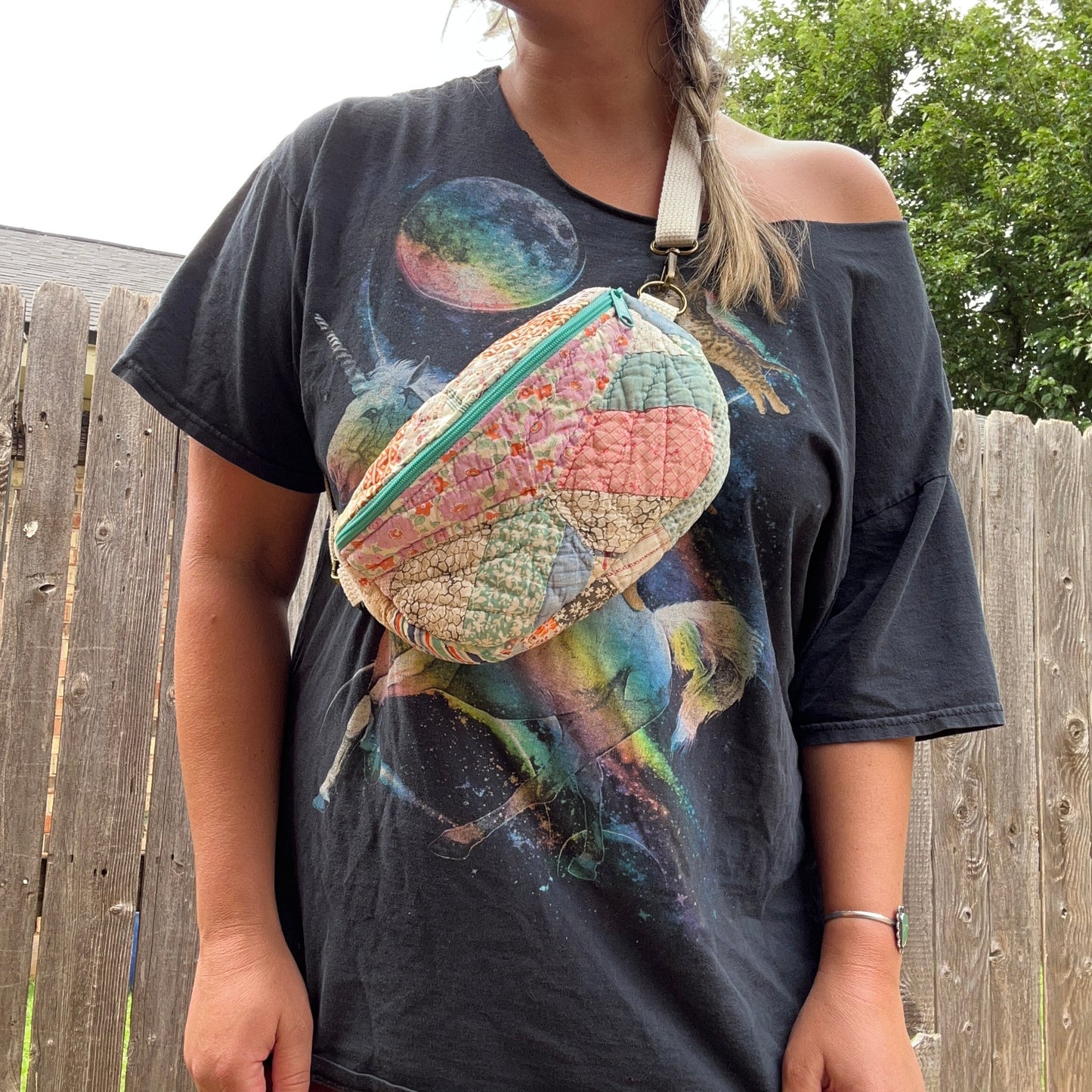 Person wearing a graphic t-shirt with a colorful bag over their shoulder outdoors.