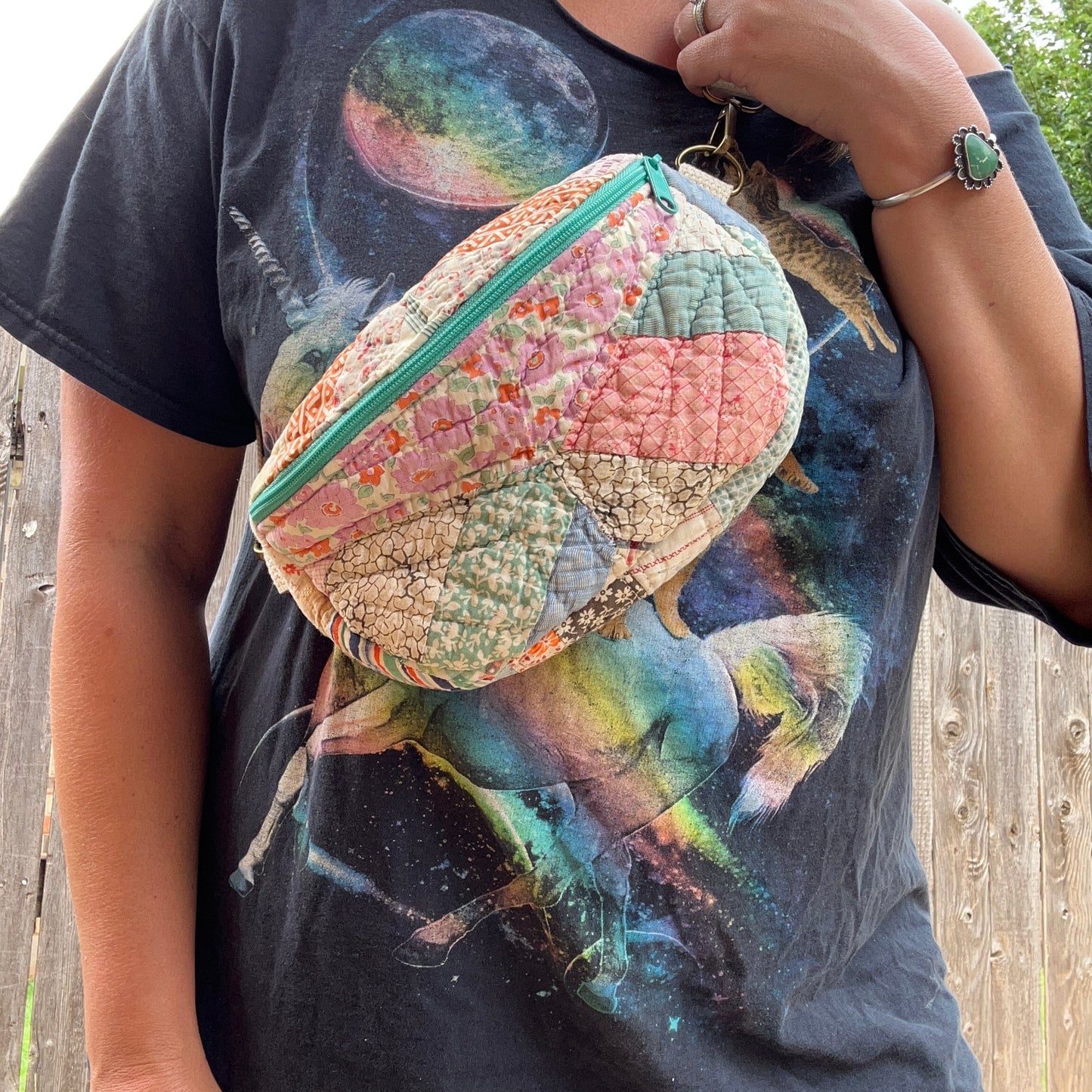 Person holding a patchwork-style pouch with a colorful design on a black t-shirt with space-themed graphics.