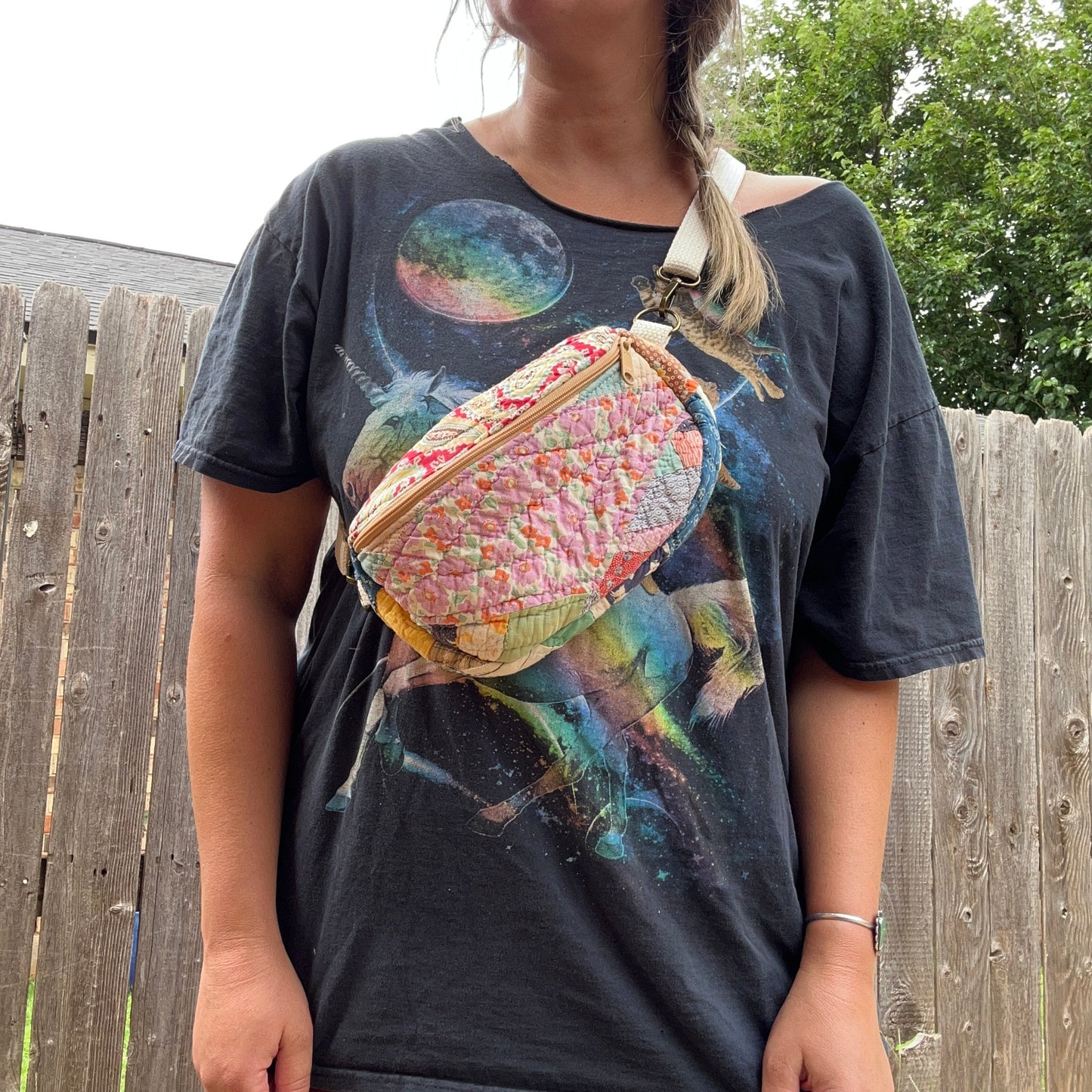 Person wearing a graphic t-shirt with a colorful bag over their shoulder outdoors.