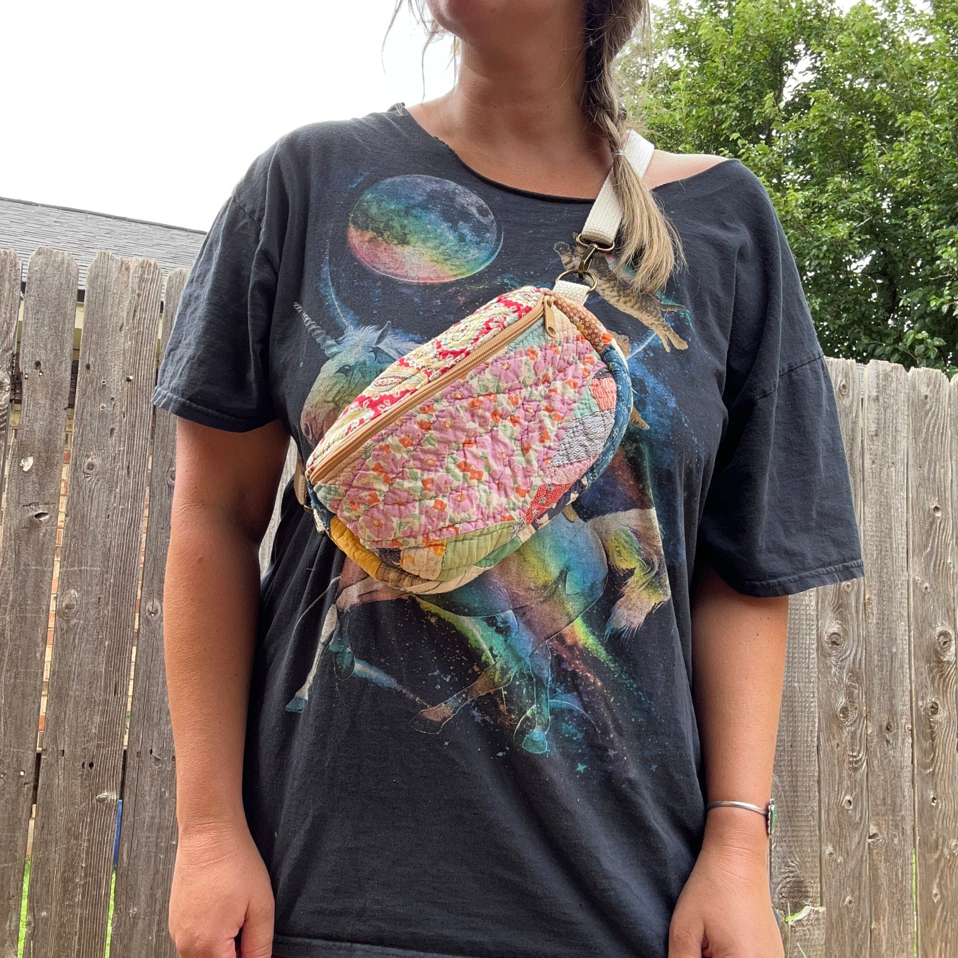 Person wearing a graphic t-shirt with a colorful bag over their shoulder outdoors.