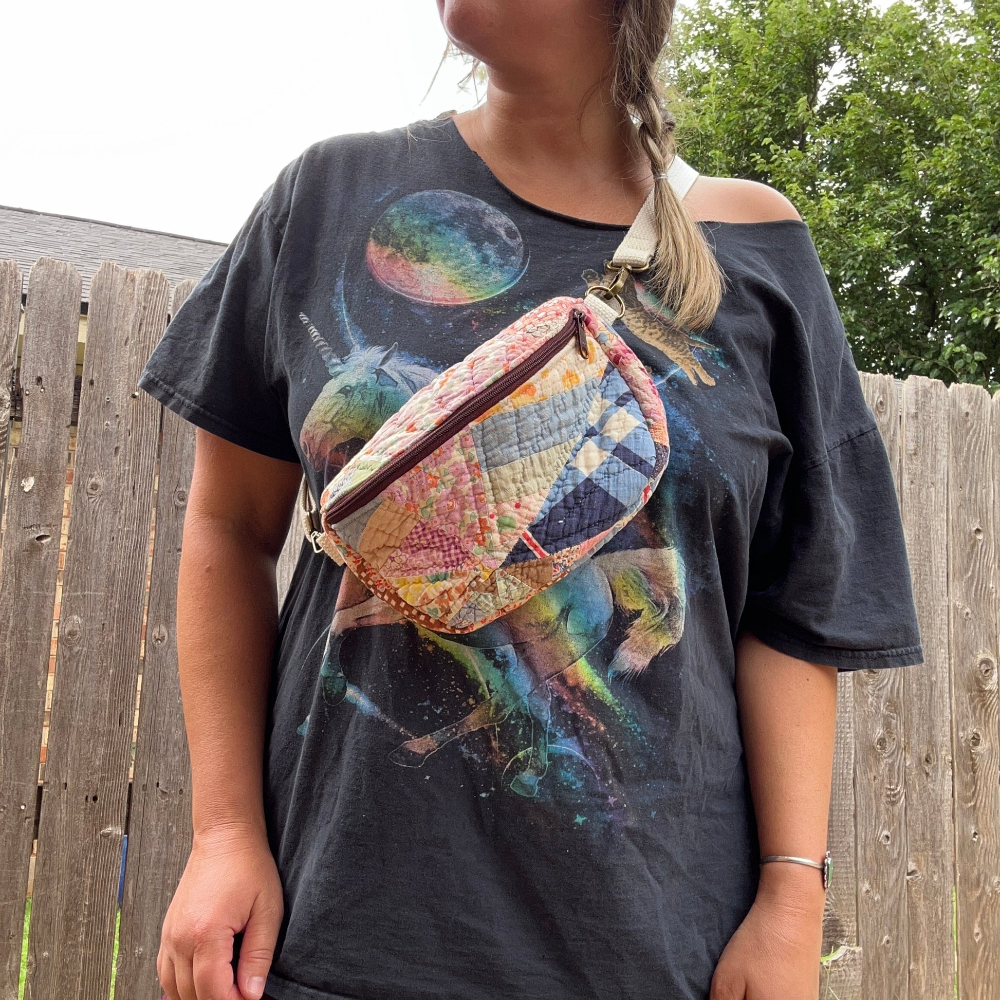 Person wearing a graphic t-shirt with a colorful bag over shoulder outdoors.