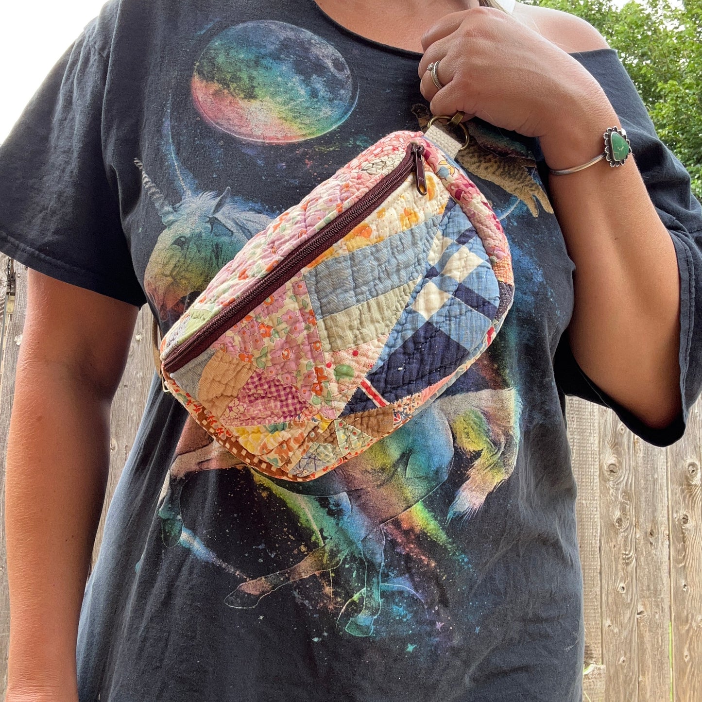 Person holding a colorful quilted bag wearing a graphic t-shirt with space-themed design.