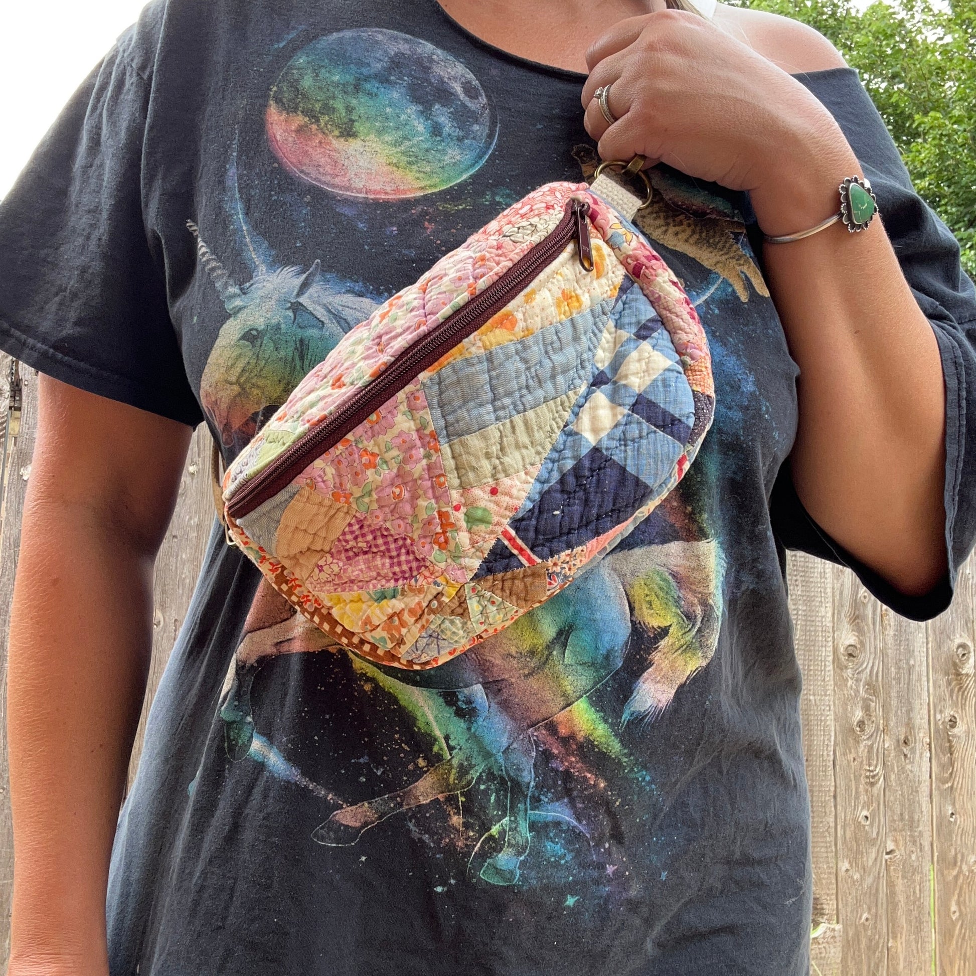 Person holding a colorful quilted bag wearing a graphic t-shirt with space-themed design.