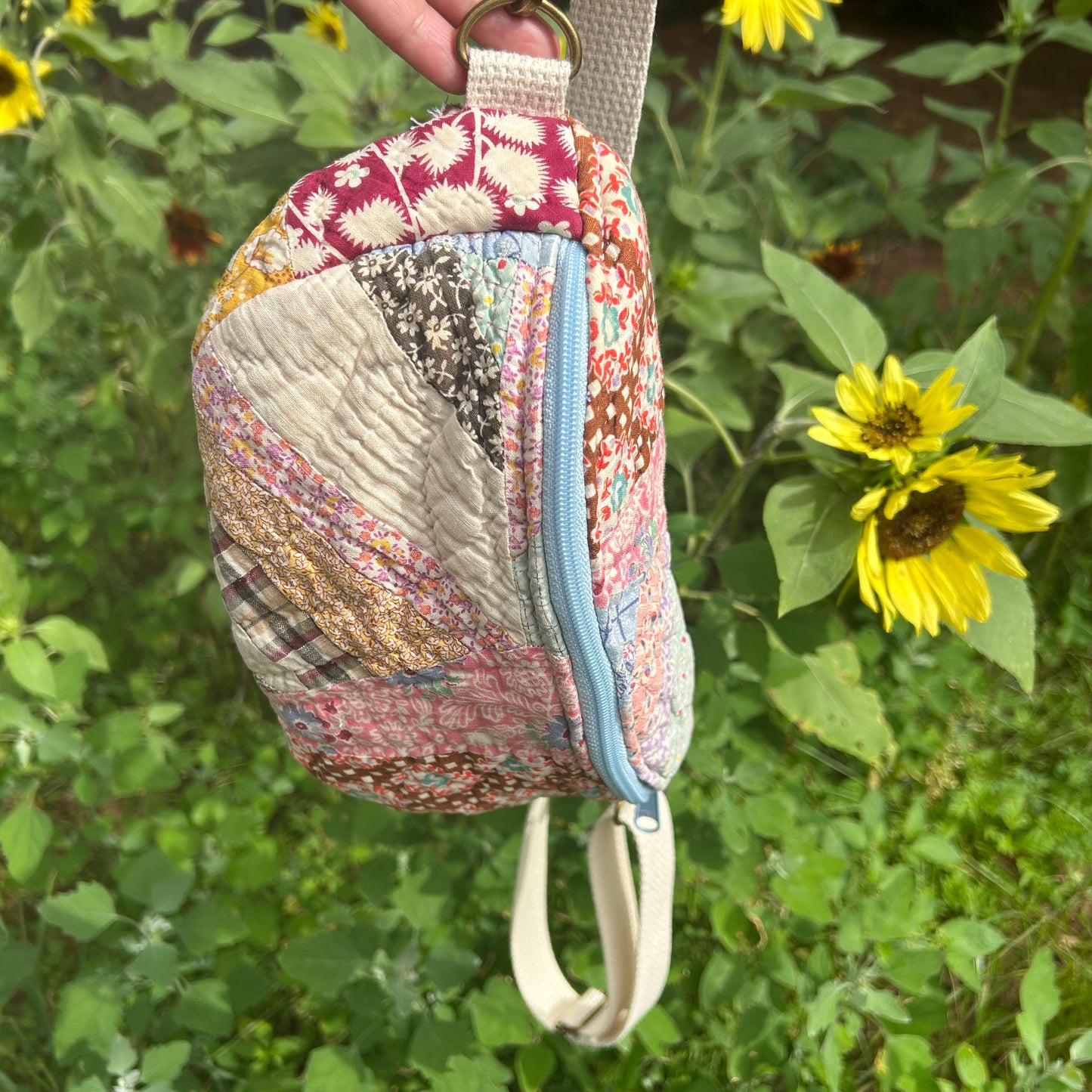 Patchwork-style pouch with floral pattern held in front of sunflowers