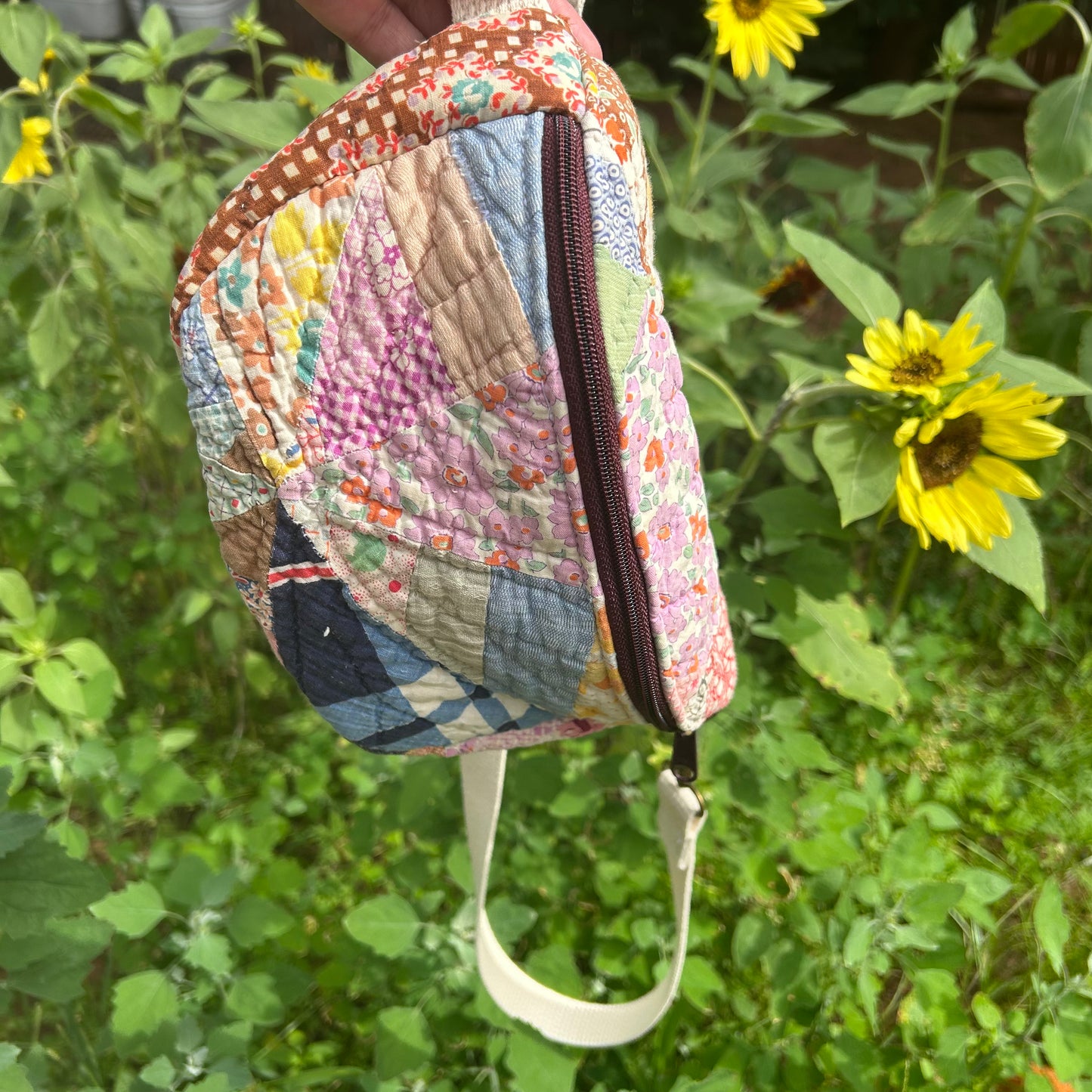 Quilted pouch with a zipper held in front of sunflowers