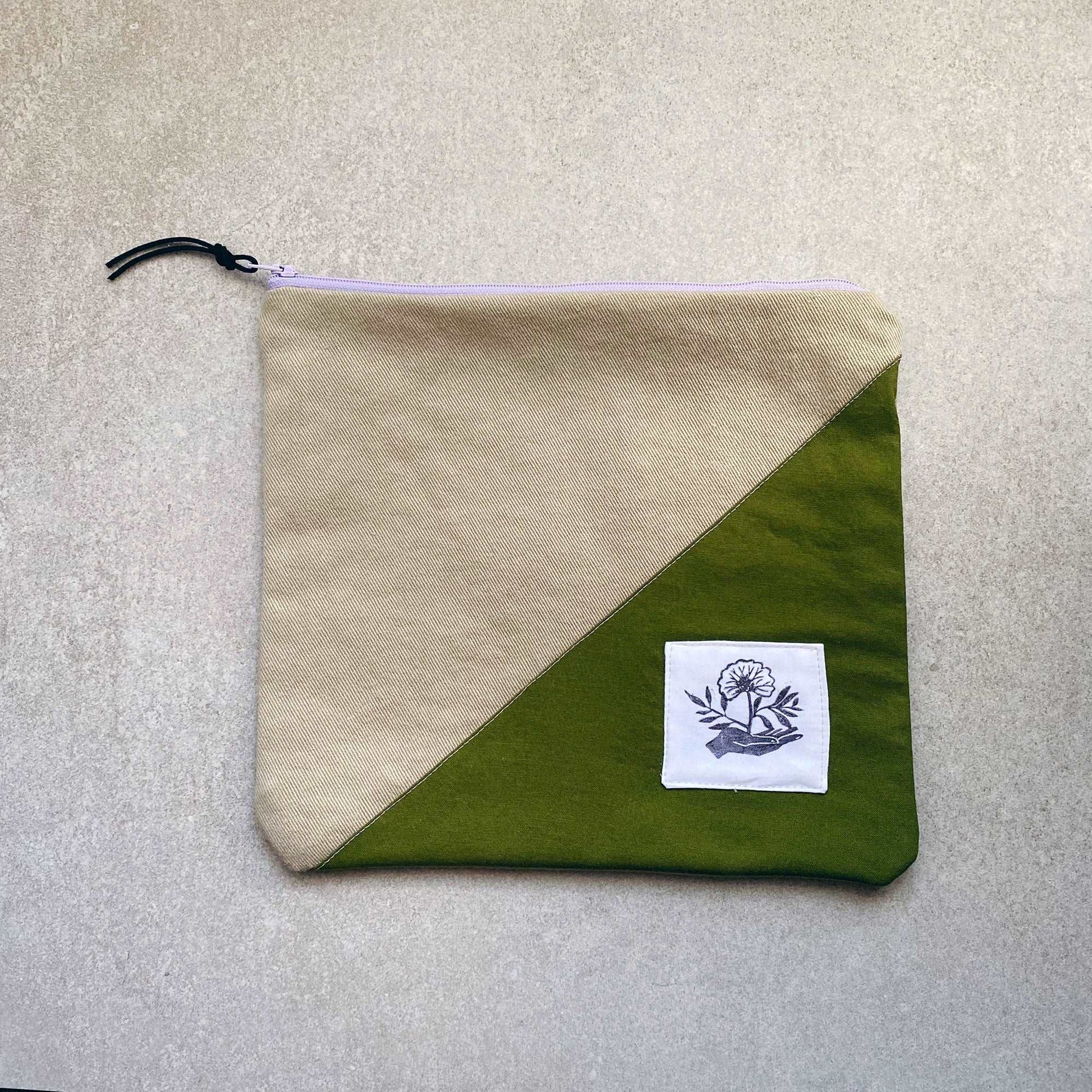 This is a photo of a large canvas zipper pouch with an olive green fabric panel. It is laying on a light gray background.