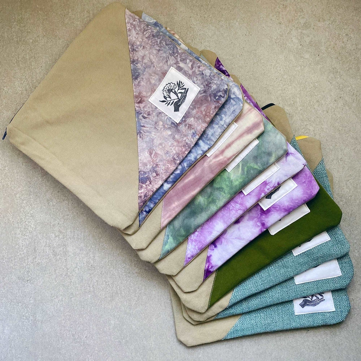 This is a photo of multiple canvas zip bags. Each bag is a little different, with fabric panels made from tie dyed fabric, solid fabric and textured fabric. Each bag includes a handprinted patch made by Sunny Chan of the Etsy shop moonandmountainprint. 